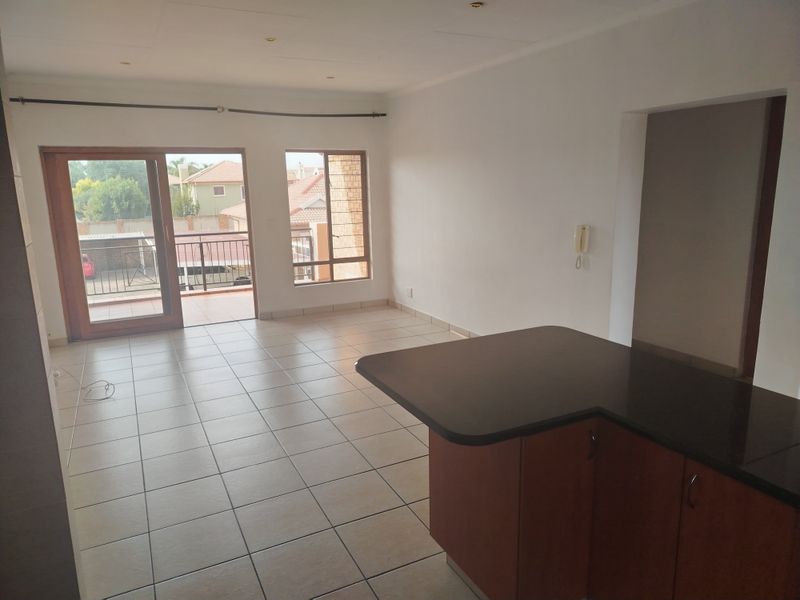 An open-plan living and kitchen area featuring tiled floors, a kitchen island with dark countertops, and sliding doors leading to a balcony.