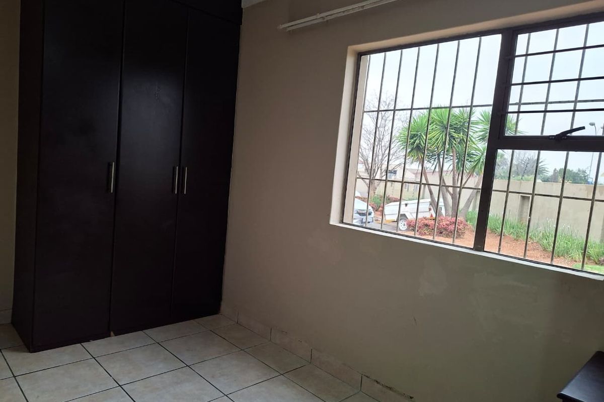 A vacant bedroom featuring tiled flooring, a dark built-in wardrobe, and a window fitted with security bars.