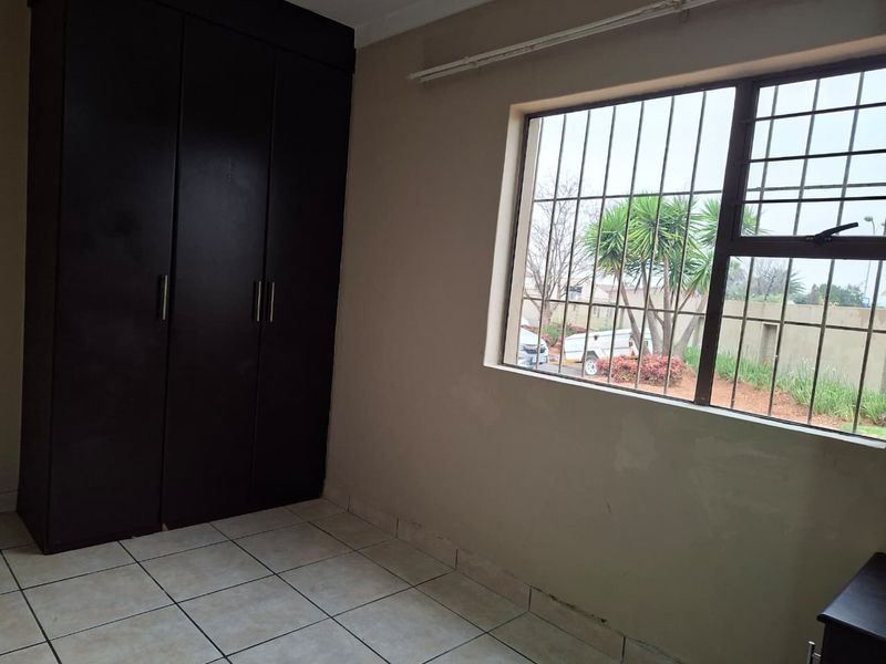 A vacant bedroom featuring tiled flooring, a dark built-in wardrobe, and a window fitted with security bars.