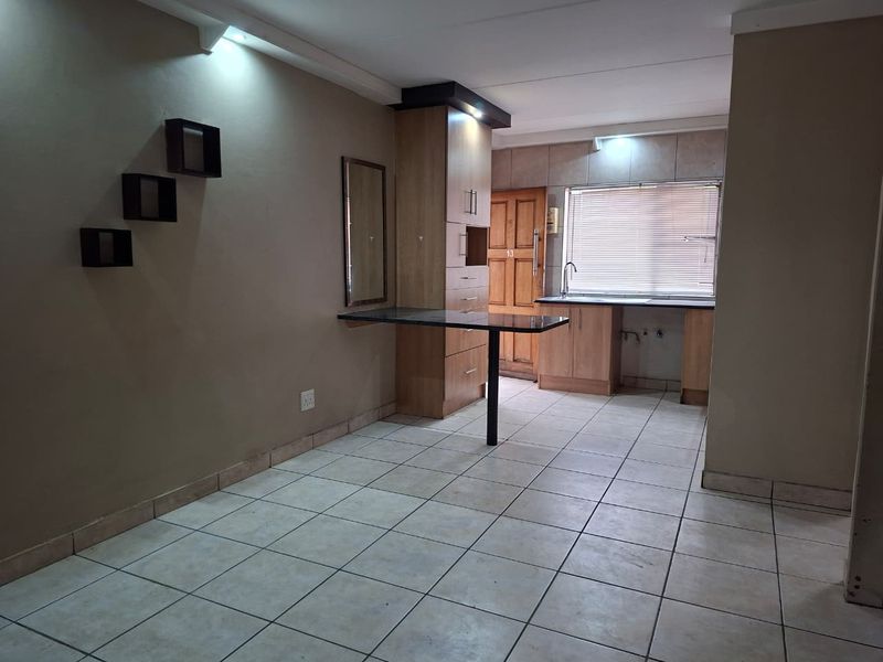 An open-plan living and kitchen area featuring tiled flooring, built-in cabinetry, and a functional kitchen workspace with a sink.
