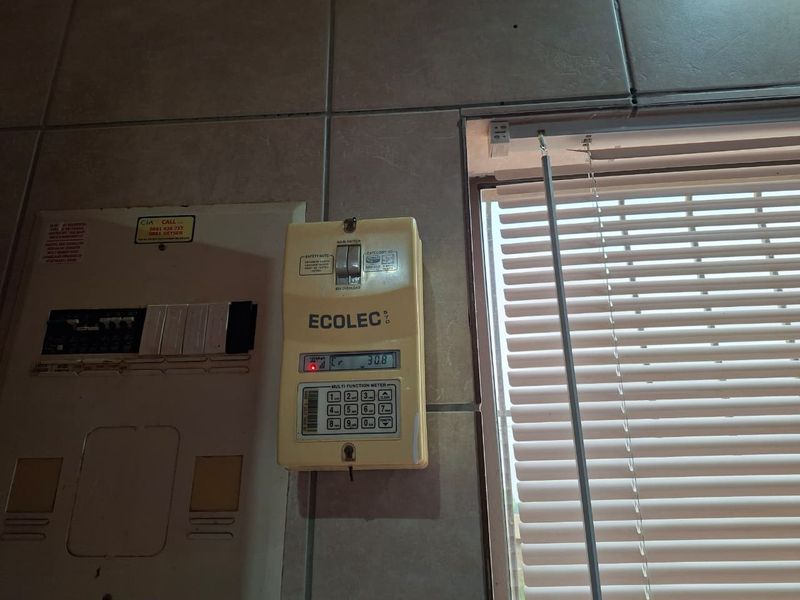 A utility area featuring a wall-mounted prepaid electricity meter and electrical distribution board, finished with ceramic wall tiles and venetian blinds.