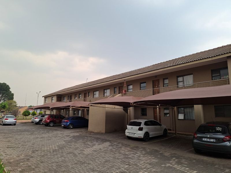 Exterior view of a multi-story apartment complex featuring paved parking areas with shade cloth carports and balcony access for upper-level units.