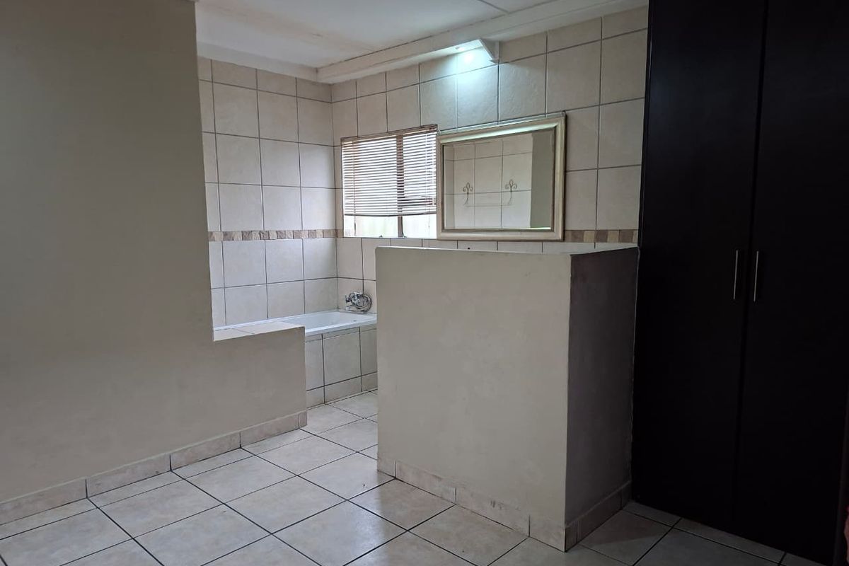 An open-plan bathroom featuring a built-in bathtub, tiled finishes, and a large built-in cupboard for storage.