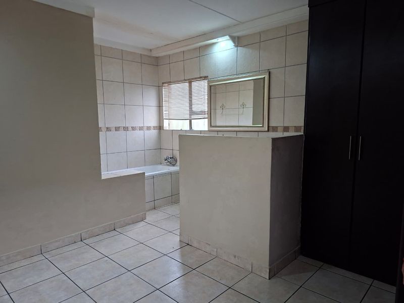 An open-plan bathroom featuring a built-in bathtub, tiled finishes, and a large built-in cupboard for storage.