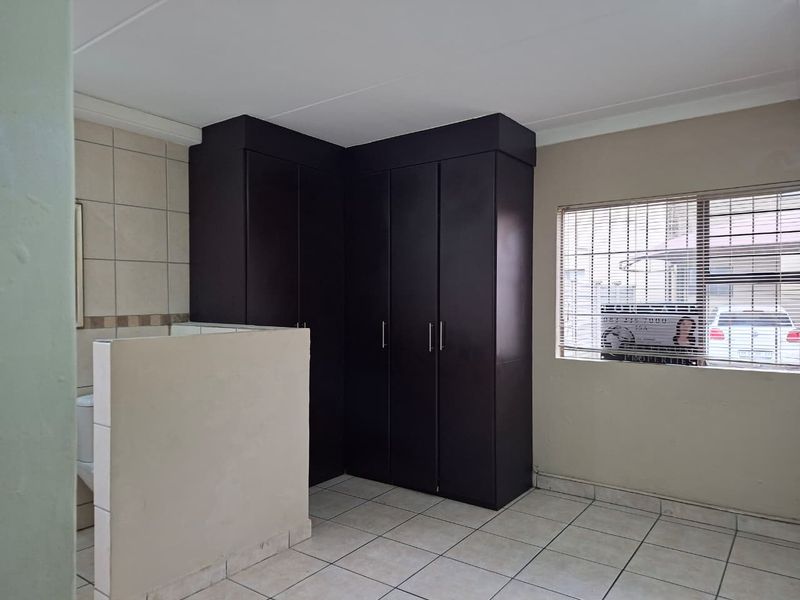 A bedroom featuring built-in dark wood cupboards, tiled flooring, and a partial partition wall, with security bars on the window.