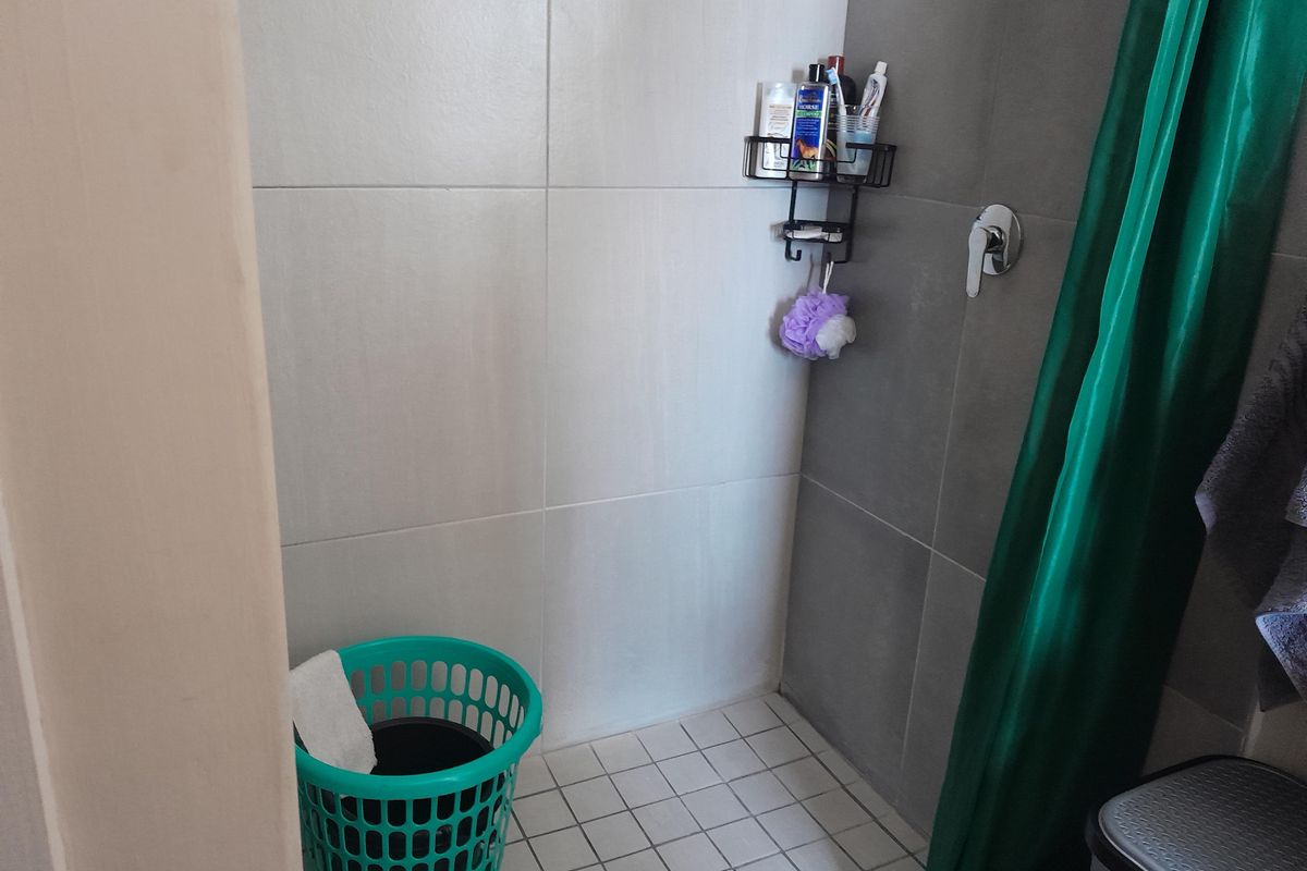 A functional shower area featuring neutral wall tiling, a floor drain, and a chrome shower mixer tap.