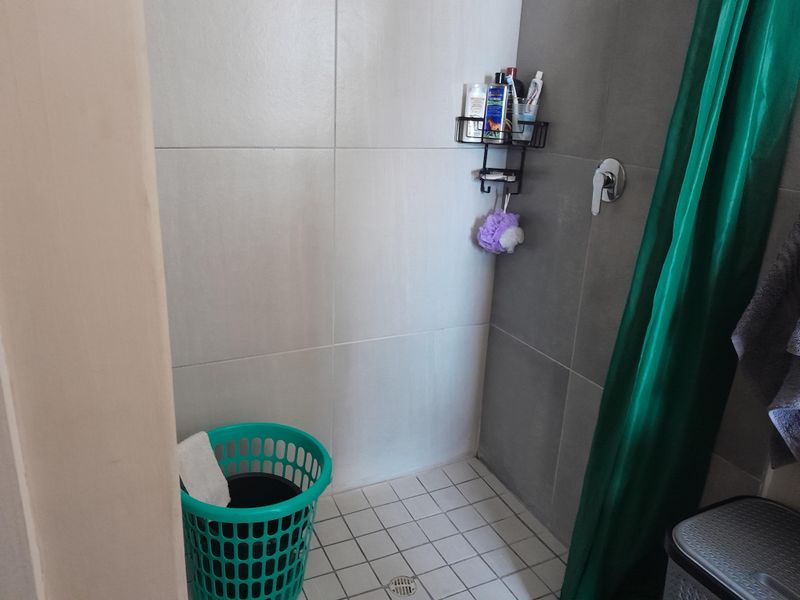 A functional shower area featuring neutral wall tiling, a floor drain, and a chrome shower mixer tap.