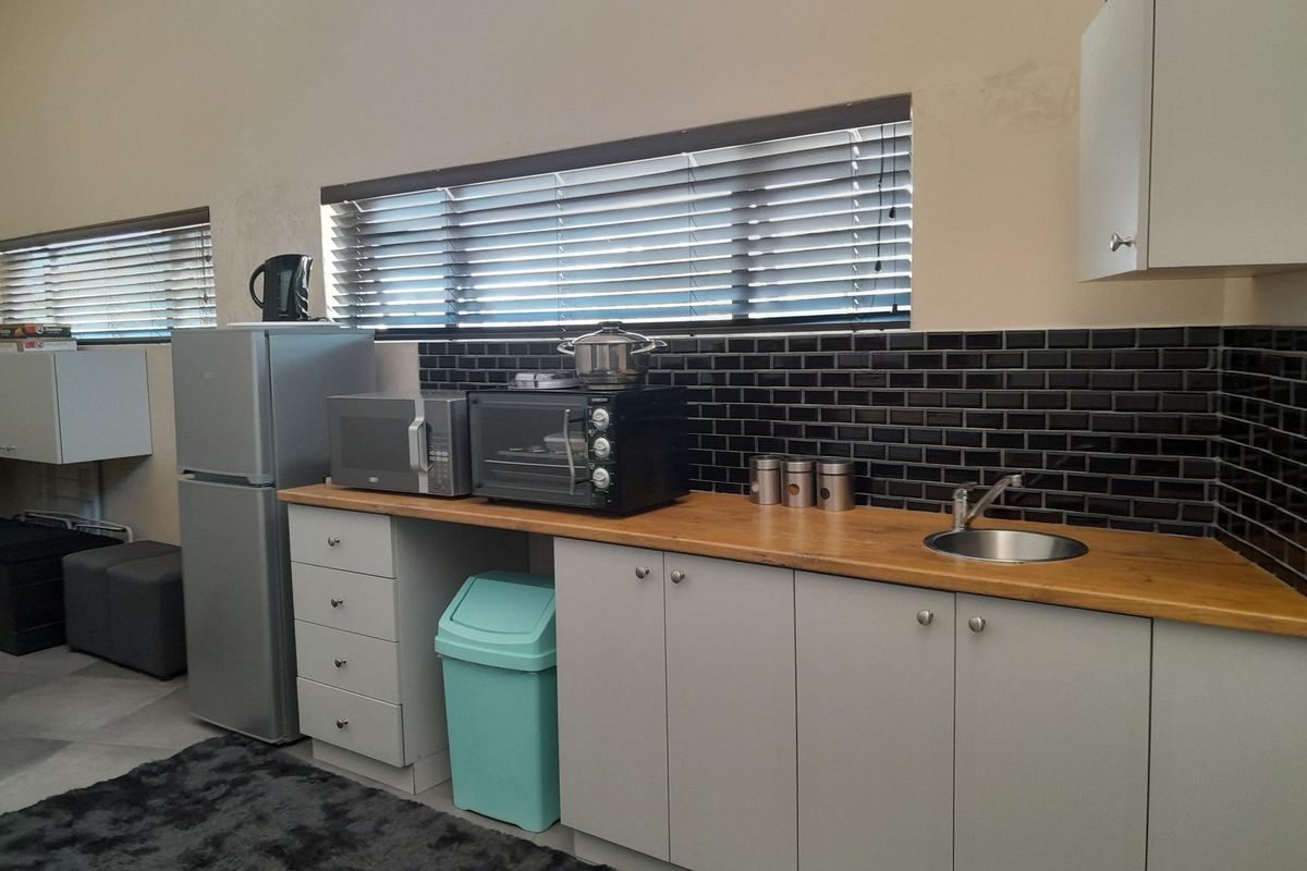 A compact kitchen area featuring a wooden countertop, subway tile backsplash, stainless steel sink, and built-in cabinetry with modern grey finishes.