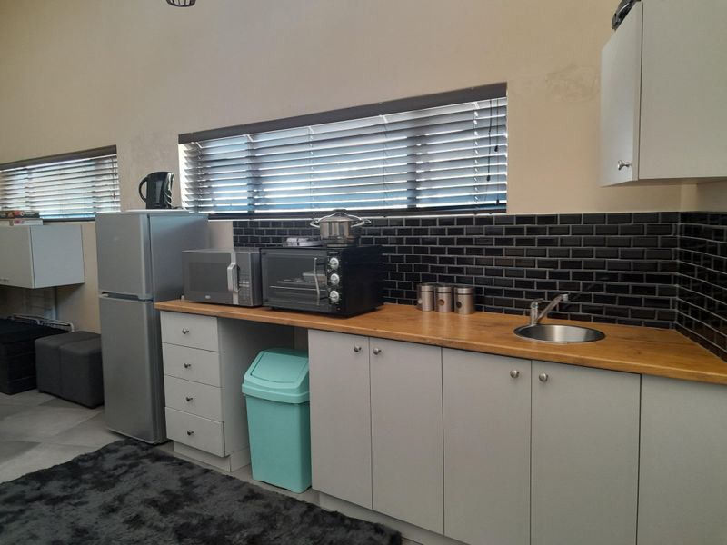 A compact kitchen area featuring a wooden countertop, subway tile backsplash, stainless steel sink, and built-in cabinetry with modern grey finishes.