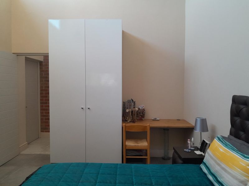 A bedroom featuring a white built-in wardrobe and a functional built-in desk area with neutral wall finishes.