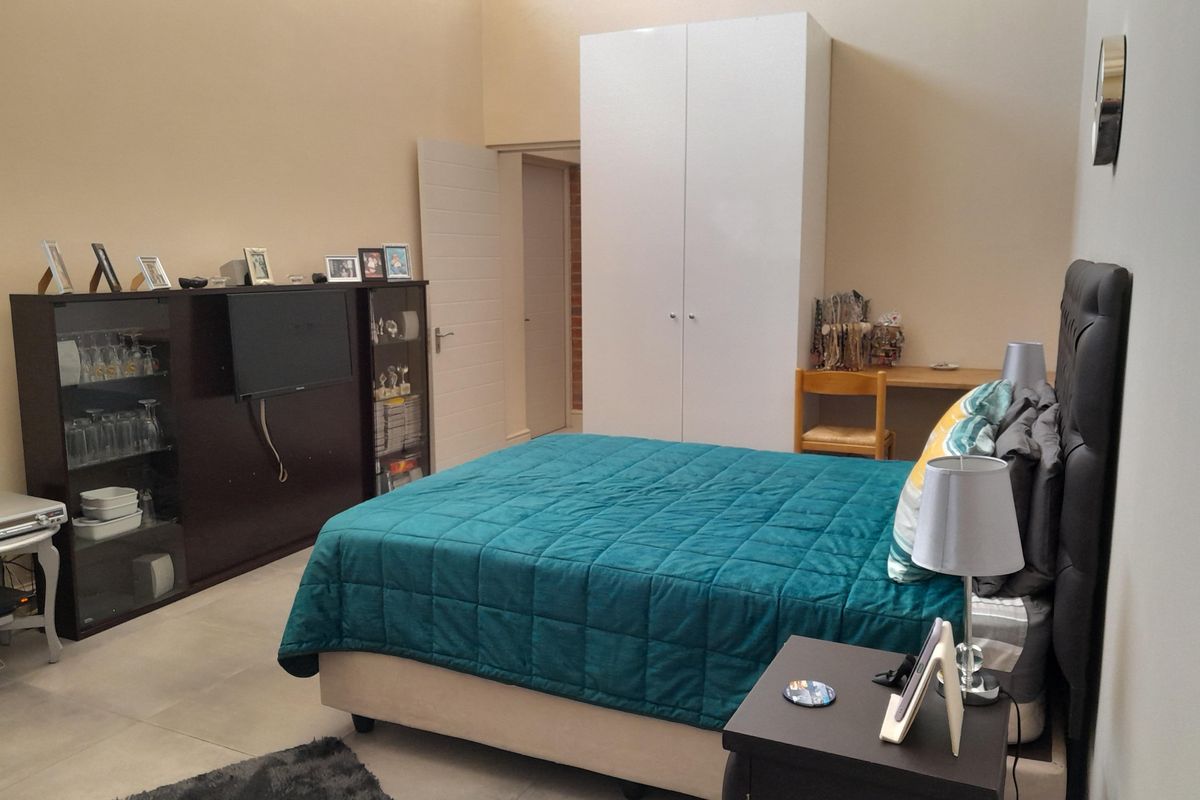 A spacious bedroom featuring neutral walls, tiled flooring, and a large built-in wardrobe, offering a clean and functional living space.