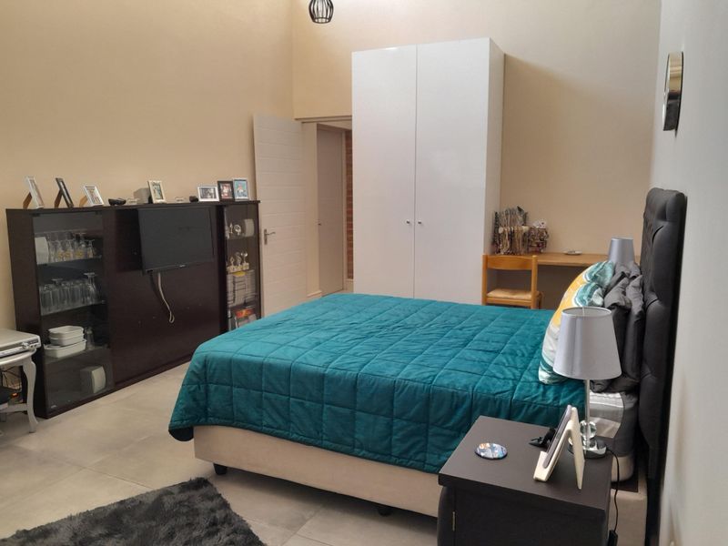 A spacious bedroom featuring neutral walls, tiled flooring, and a large built-in wardrobe, offering a clean and functional living space.