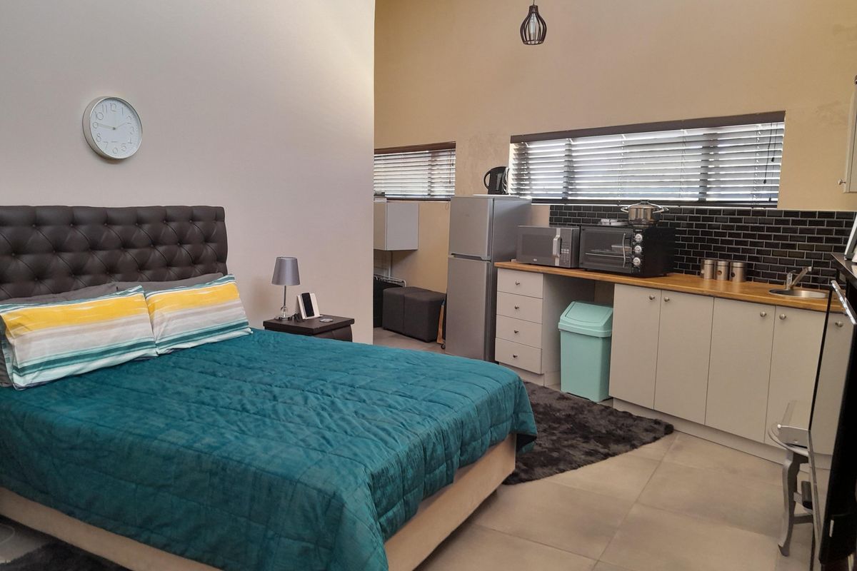 Open-plan studio apartment featuring a combined bedroom and kitchenette area with modern cabinetry, subway tile backsplash, and neutral tiled flooring.