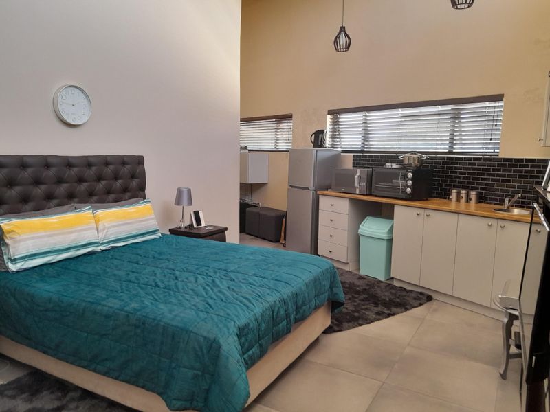 Open-plan studio apartment featuring a combined bedroom and kitchenette area with modern cabinetry, subway tile backsplash, and neutral tiled flooring.