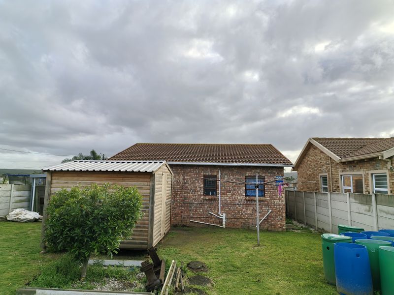 Rear view of the property featuring a brick exterior, tiled roof, a wooden garden shed, and a precast concrete boundary wall.