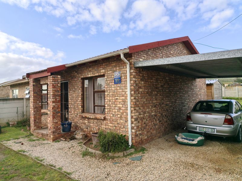 A single-story face brick house featuring a covered carport, metal roofing, and a gravel driveway area.