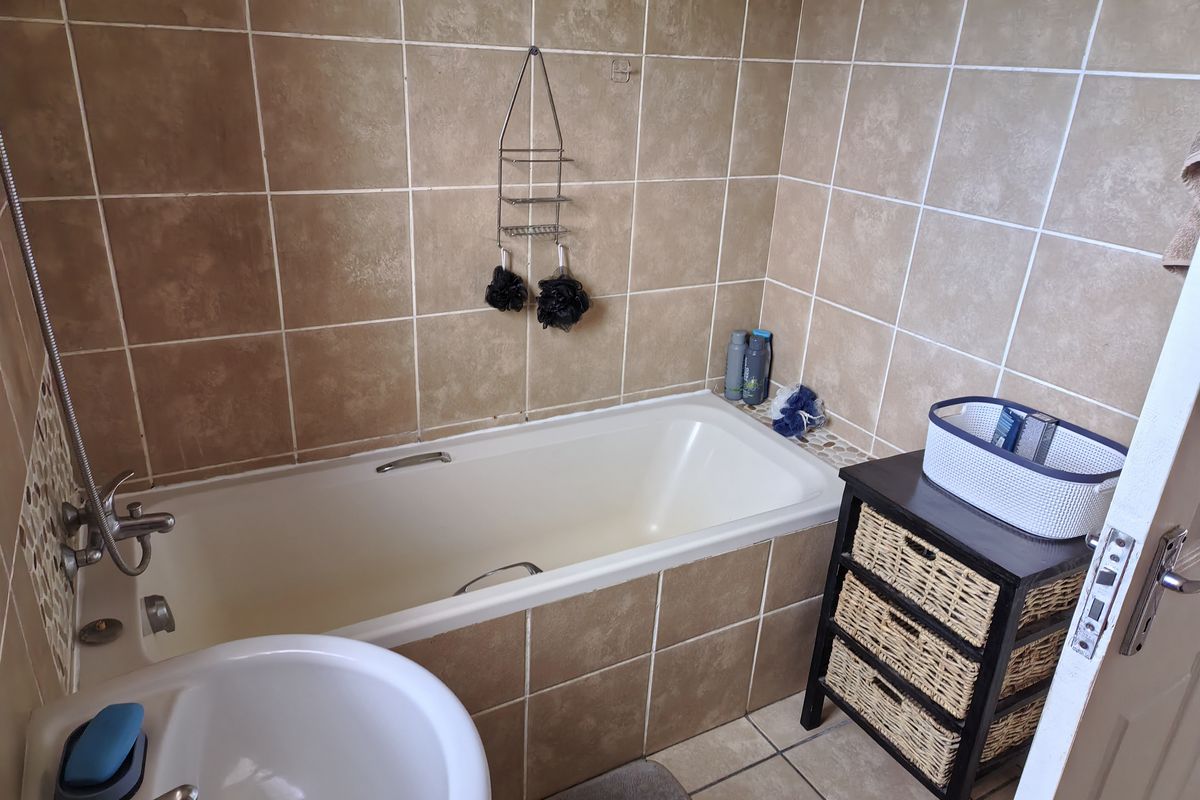 A functional bathroom featuring a built-in bathtub with tiled surround and neutral ceramic wall and floor tiles.