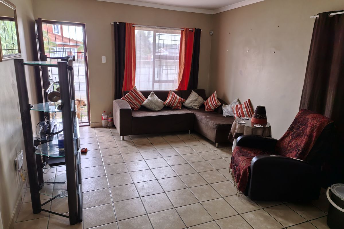 A living room featuring tiled flooring, a sliding door with security gate, and neutral wall paint, offering a functional space for relaxation.