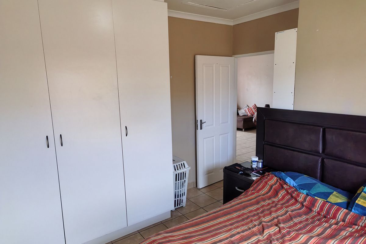 A bedroom featuring built-in cupboards, tiled flooring, and neutral wall tones, offering a functional space with direct access to an adjacent room.