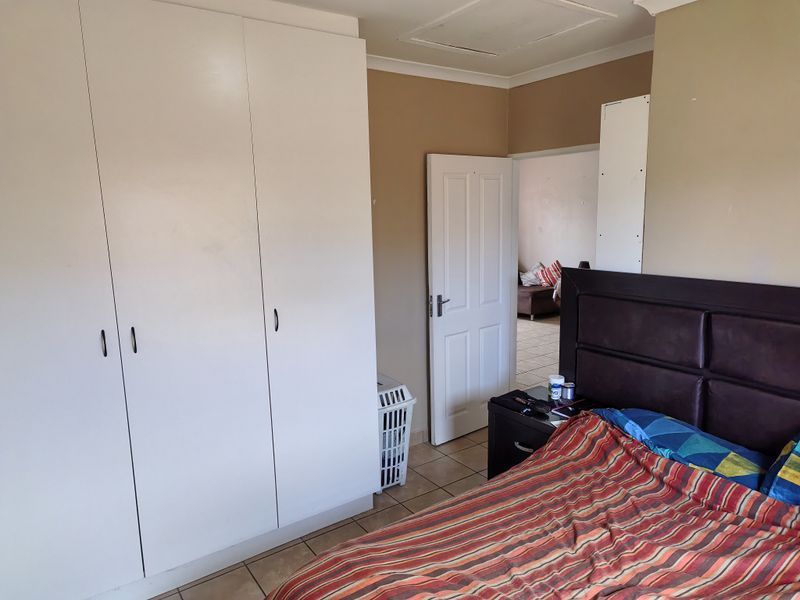 A bedroom featuring built-in cupboards, tiled flooring, and neutral wall tones, offering a functional space with direct access to an adjacent room.