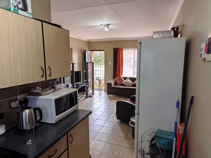 Open-plan kitchen and living area featuring tiled flooring, laminate cabinetry, and direct access to an outdoor space through a security gate.