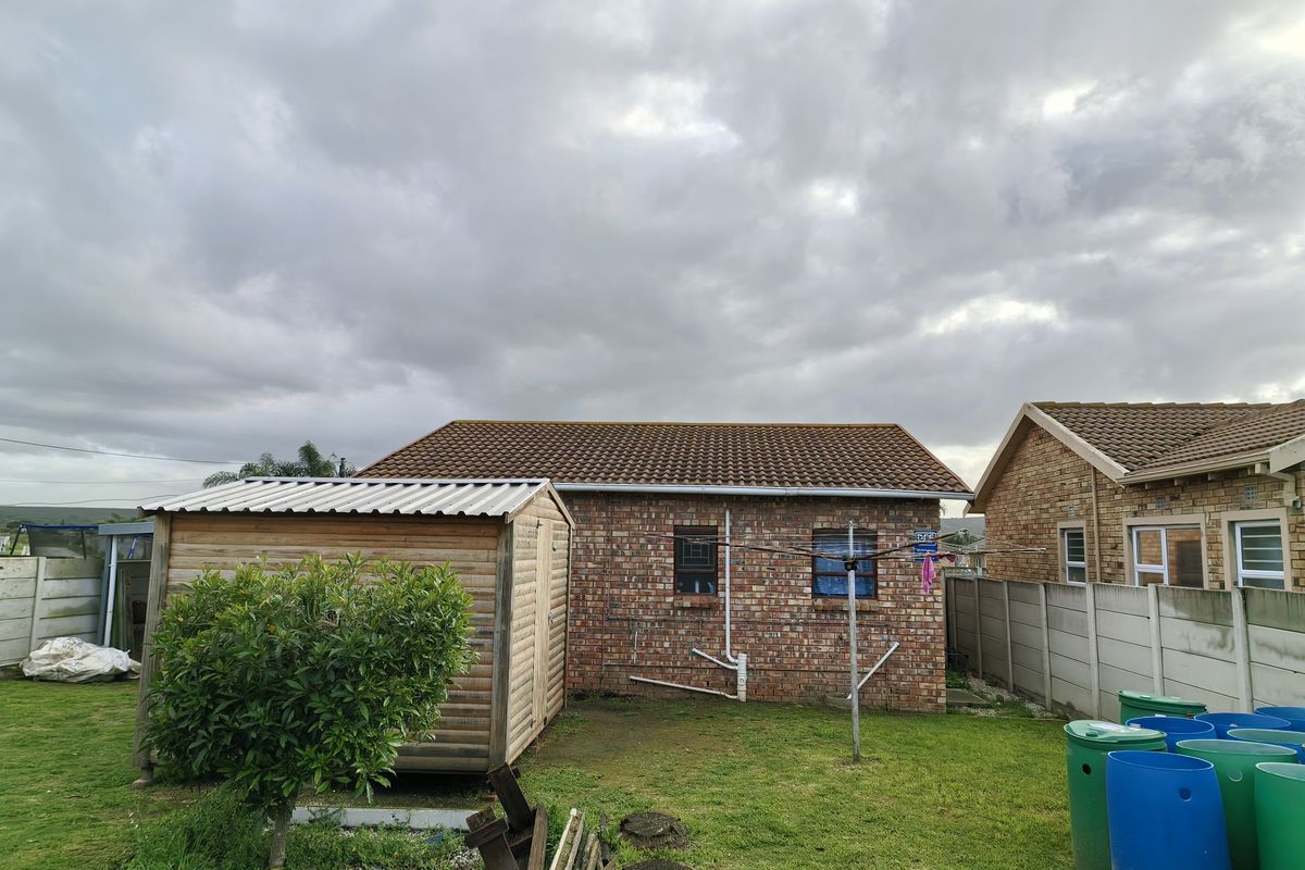 Rear view of the property featuring a brick exterior, tiled roof, a wooden garden shed, and a precast concrete boundary wall.