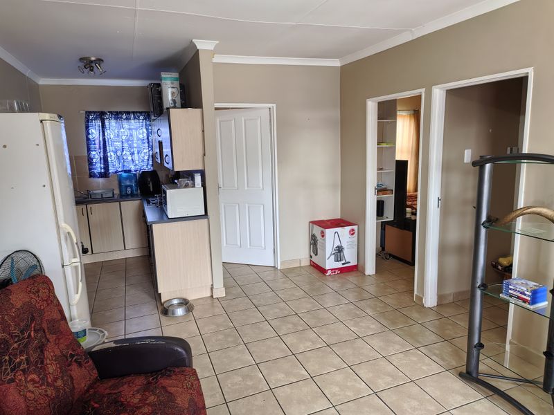 Open plan living area featuring tiled flooring and a compact kitchen with built-in cabinetry, providing access to adjacent rooms.