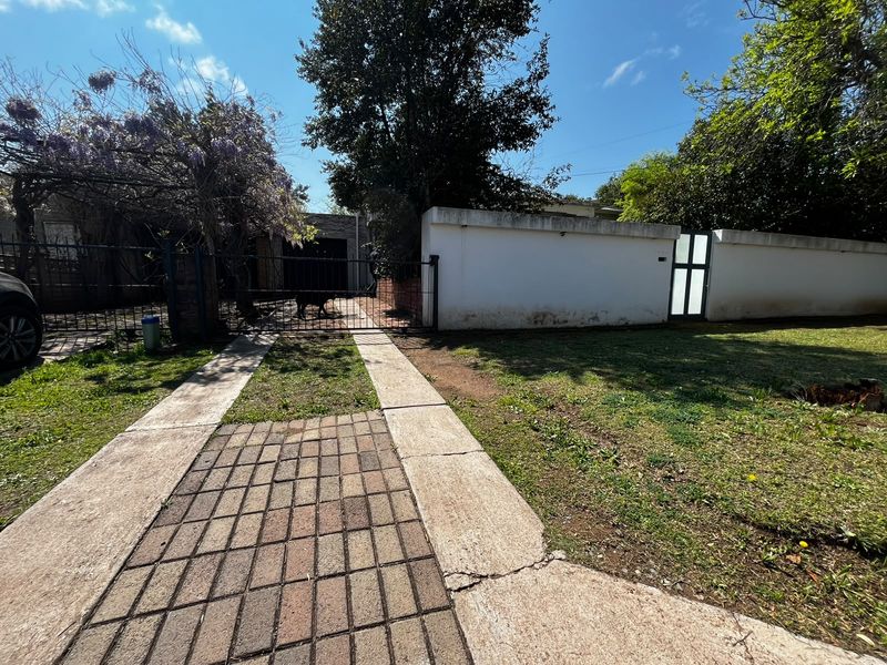 Front exterior view of the property featuring a paved driveway, perimeter wall, and gated entrance with established garden area.