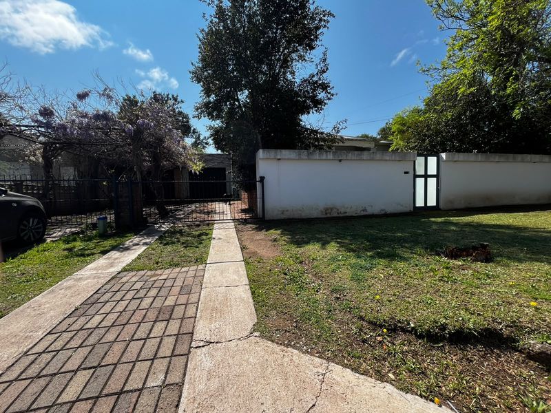 Front exterior view of the property featuring a paved driveway, concrete walkway, perimeter wall, and gated entrance.