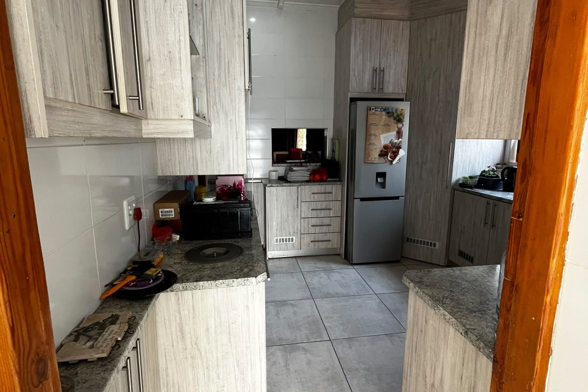 A functional galley-style kitchen featuring light wood-grain cabinetry, stone-look laminate countertops, and neutral floor tiles.
