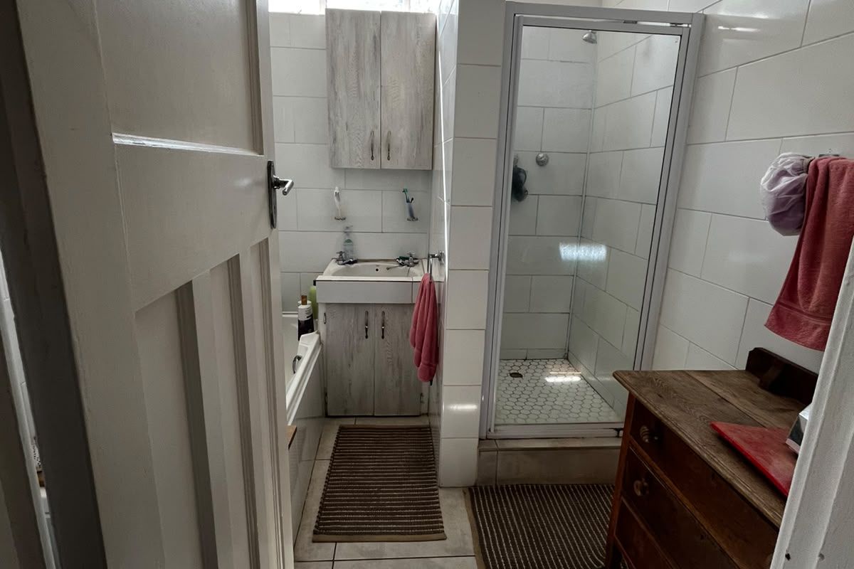A functional bathroom featuring a shower enclosure, vanity basin, and tiled finishes, currently showing signs of ceiling wear and requiring cosmetic updates.