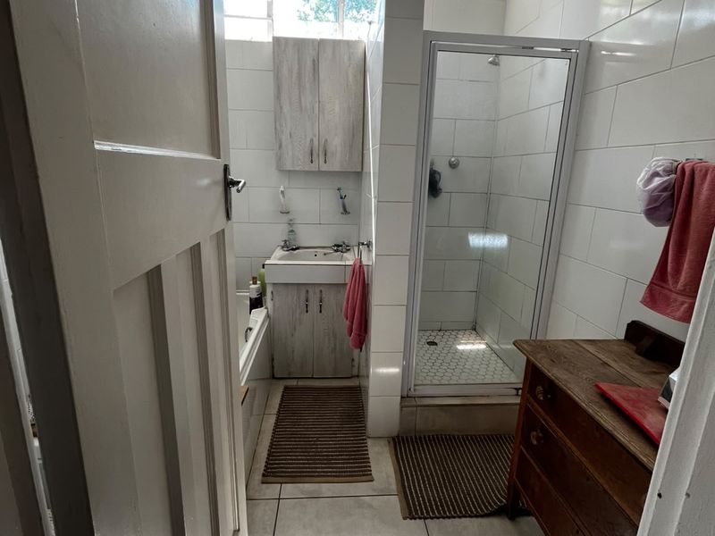 A functional bathroom featuring a shower enclosure, vanity basin, and tiled finishes, currently showing signs of ceiling wear and requiring cosmetic updates.