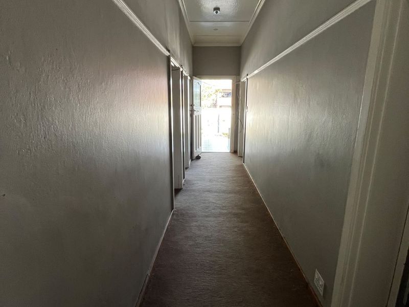 A long, empty hallway featuring a drop ceiling, picture rails, and carpet flooring, leading towards an exterior doorway.