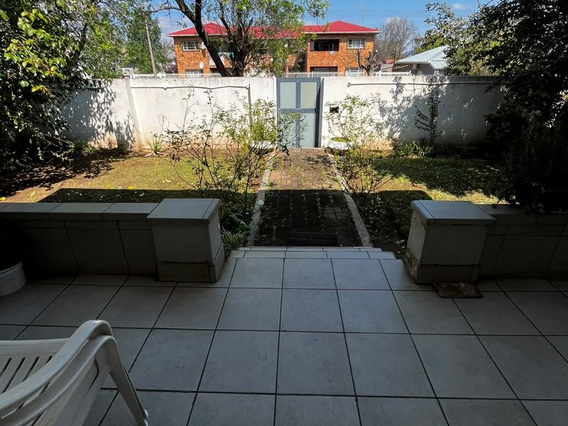 A tiled patio area overlooking a private garden with a paved pathway and secure perimeter wall.