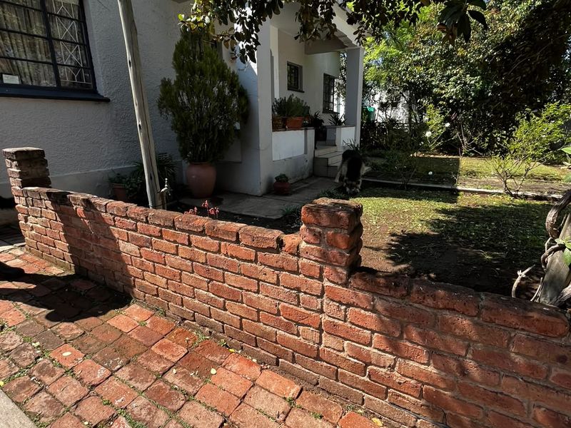 Front exterior view featuring a brick boundary wall, paved driveway, and a covered porch entrance to the residence.