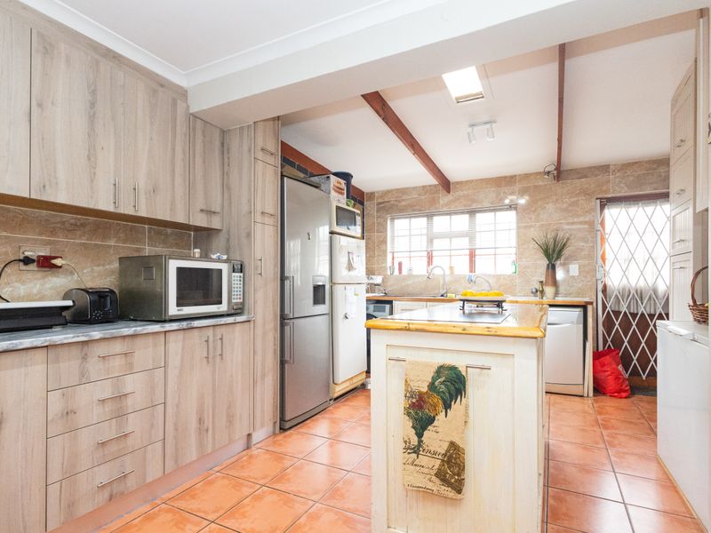 A functional kitchen featuring wood-look cabinetry, a central island, tiled flooring, and a skylight, providing ample workspace and natural light.
