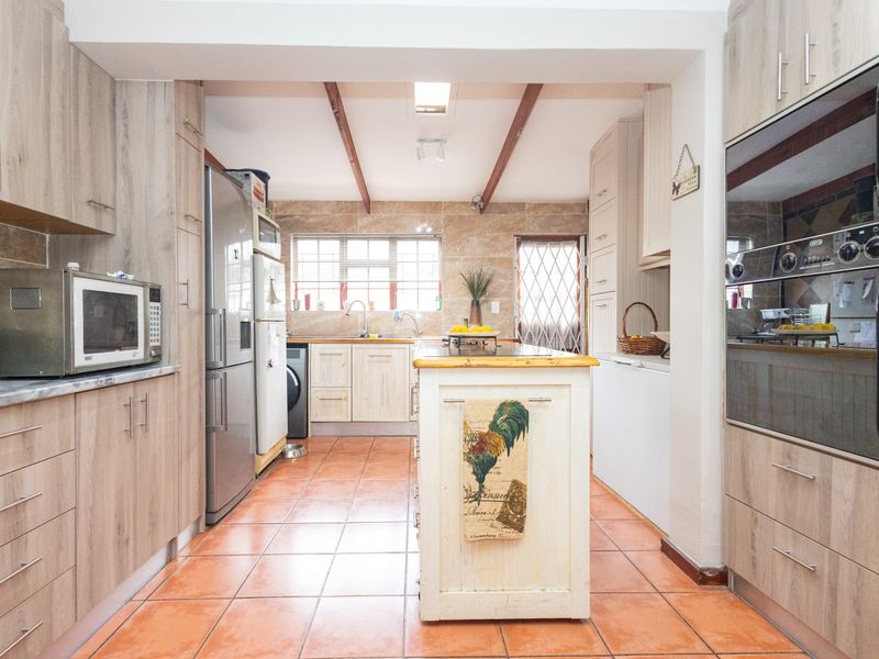 Spacious kitchen featuring wood-look cabinetry, a central island, double wall ovens, and tiled flooring with exposed ceiling beams.