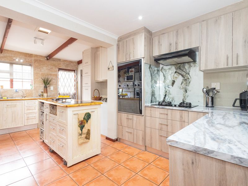 A well-appointed kitchen featuring light wood-grain cabinetry, marble-effect countertops and splashbacks, built-in oven, gas hob, and tiled flooring.