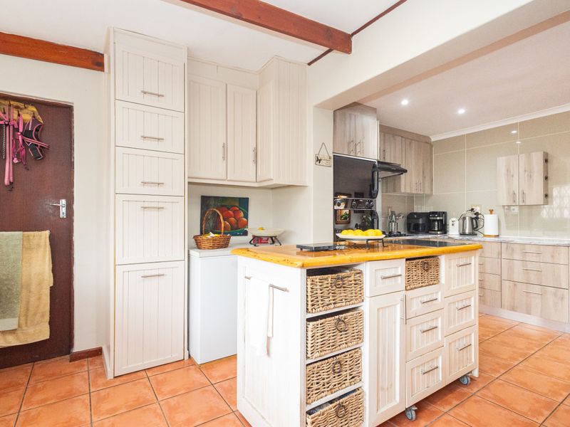 A functional kitchen featuring tiled flooring, exposed timber ceiling beams, ample built-in cabinetry, and a central kitchen island with integrated storage.