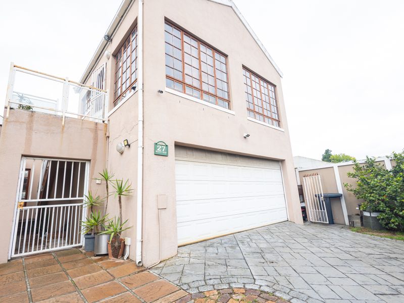 Front elevation of a two-story house featuring a double garage, paved driveway, and an upper-level balcony with security gates.