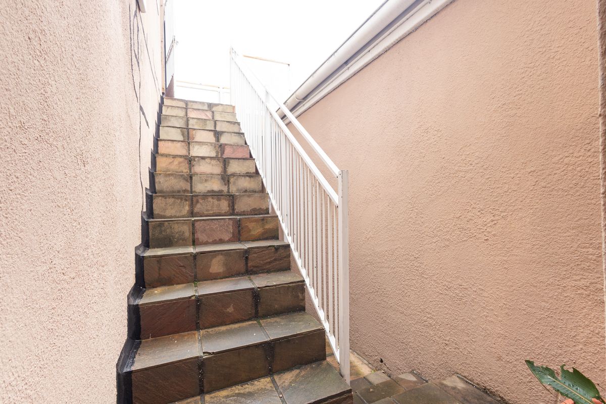 An exterior stone staircase with a metal handrail leading to an upper level, featuring textured walls and visible wear on the steps.