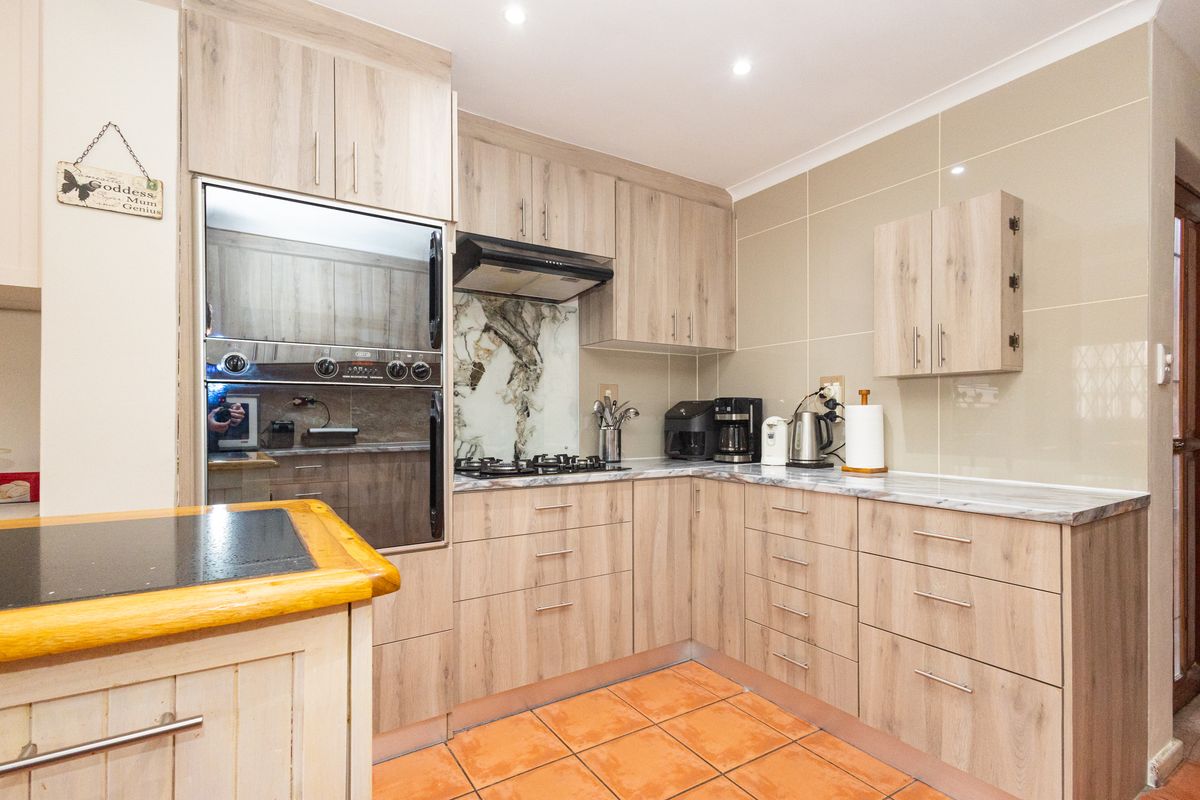 A functional kitchen featuring light wood-grain cabinetry, built-in oven, gas hob with extractor, and tiled splashbacks, offering a clean and practical workspace.