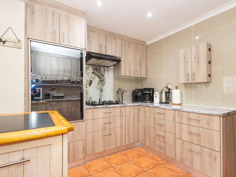 A functional kitchen featuring light wood-grain cabinetry, built-in oven, gas hob with extractor, and tiled splashbacks, offering a clean and practical workspace.