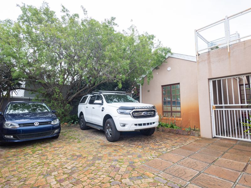 Front exterior view of the property featuring a cobblestone driveway, security gate, and a paved patio area with visible exterior wall staining.
