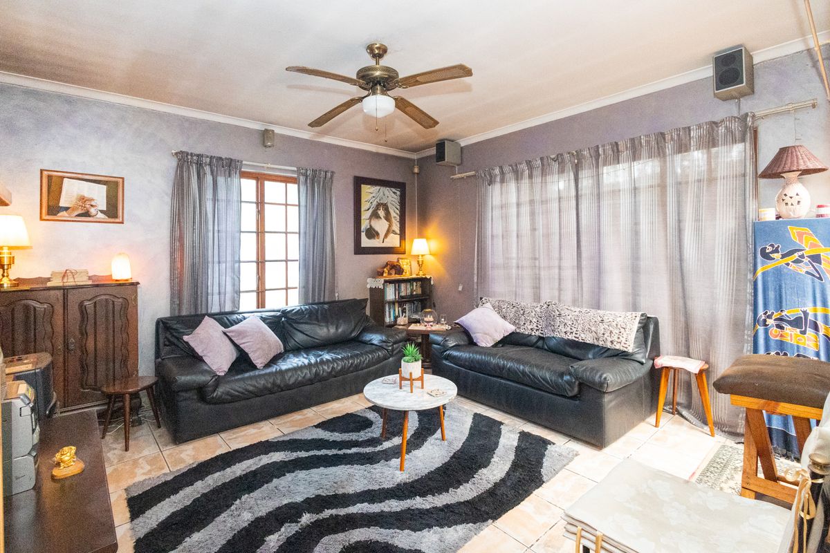 A living room featuring tiled flooring, a ceiling fan, and large windows with curtains, offering a functional space for relaxation.