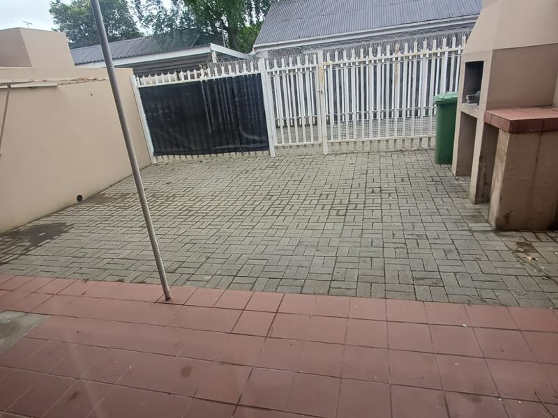 A paved outdoor patio area featuring a built-in braai, enclosed by security fencing and a metal gate, offering a functional space for outdoor entertaining.