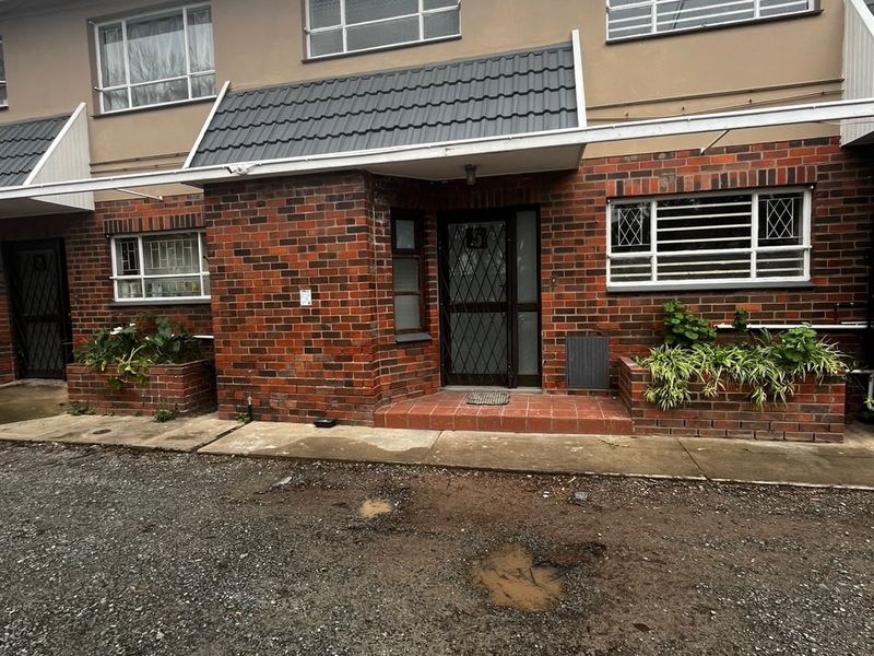 Front elevation of a brick apartment unit featuring security gates, window bars, and built-in brick planters at the entrance.