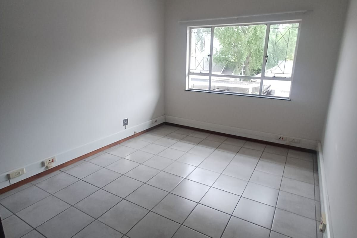 A vacant bedroom featuring neutral tiled flooring, a window with security bars, and basic electrical fixtures, offering a clean canvas for personalization.