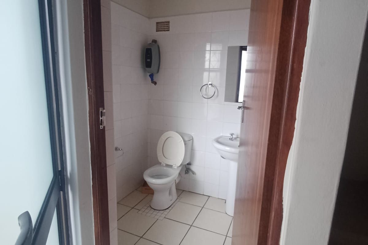 A compact bathroom featuring a pedestal basin, toilet, and tiled finishes, requiring minor updates to modernize the space.