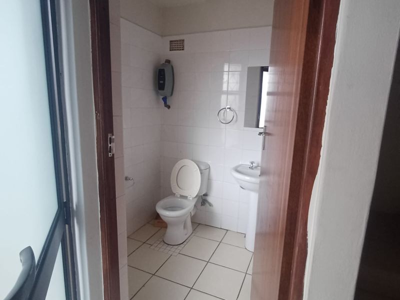 A compact bathroom featuring a pedestal basin, toilet, and tiled finishes, requiring minor updates to modernize the space.